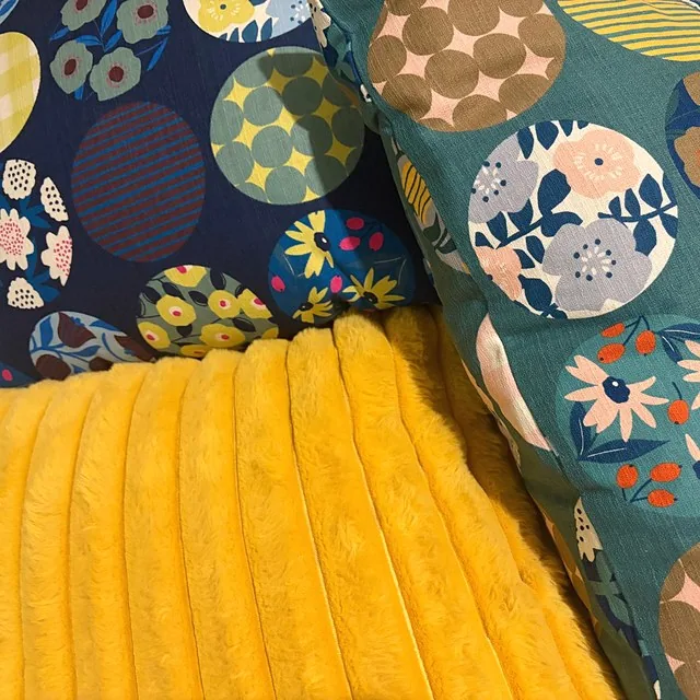 Navy and teal cushion covers resting on a soft yellow throw